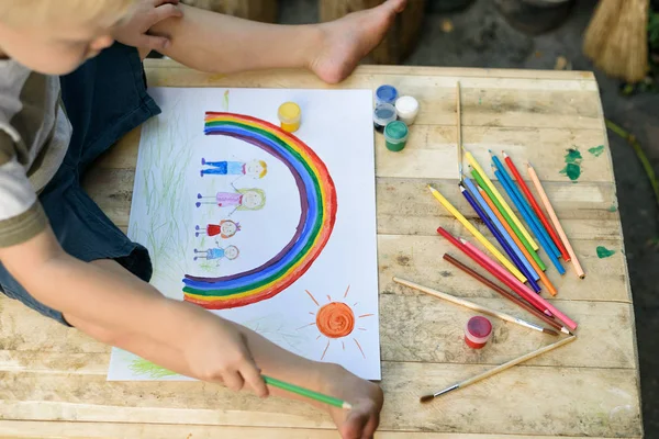 Cute boy draws rainbow and family. Open air. Top view. Creative concept.