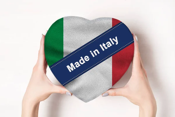 Iscrizione Made in Italy, la bandiera dell'Italia. Mani femminili che tengono una scatola a forma di cuore. Fondo bianco . — Foto Stock