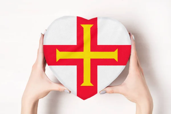 Bandeira de Guernsey em uma caixa em forma de coração em mãos femininas. Fundo branco — Fotografia de Stock
