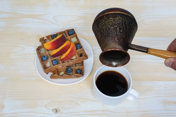 Chocolate Belgian waffles with fruits, cup of coffee and cezve on white wooden background. Delicious breakfast. Top view — Stock Photo, Image