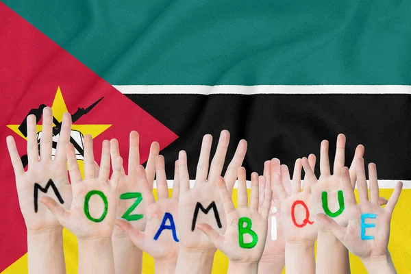 Inscripción Mozambique en las manos de los niños en el fondo de una bandera ondeante de Mozambique — Foto de Stock