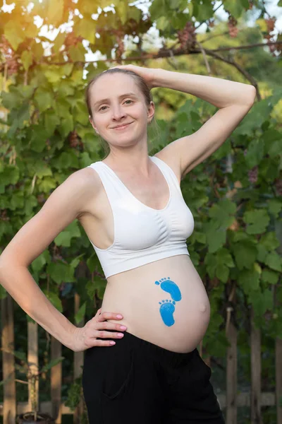 Joven mujer embarazada sonriente. Huella azul dibujando en el vientre. Concepto de embarazada . —  Fotos de Stock