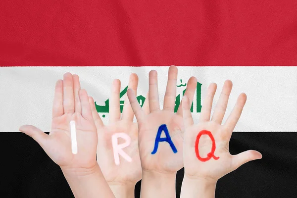 Inscripción Irak en las manos de los niños en el contexto de una bandera ondeante del Iraq — Foto de Stock
