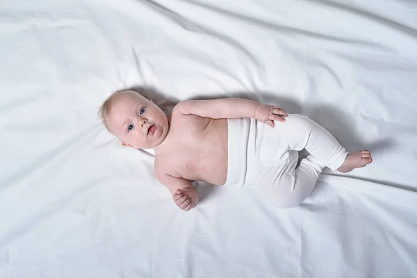 Cute blond baby with a naked torso lying on white sheets. Top view — Stock Photo, Image