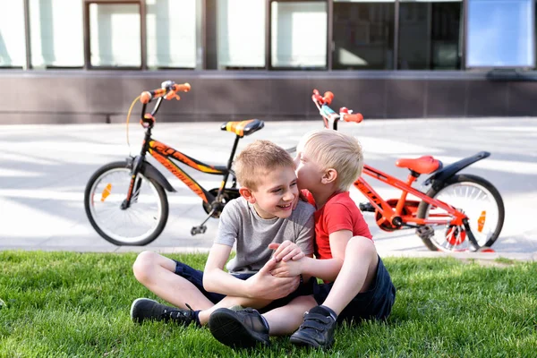 İki çocuk çimenlerin üzerinde otururken iletişim kuruyor. Bisikletten sonra dinlen, arka planda bisikletler