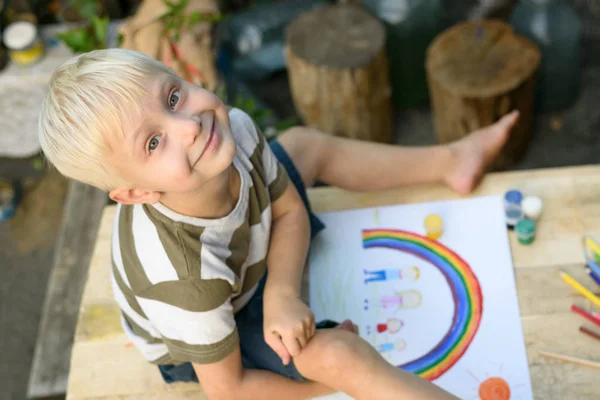Cute boy draws rainbow and family. Open air. Top view. Creative concept.