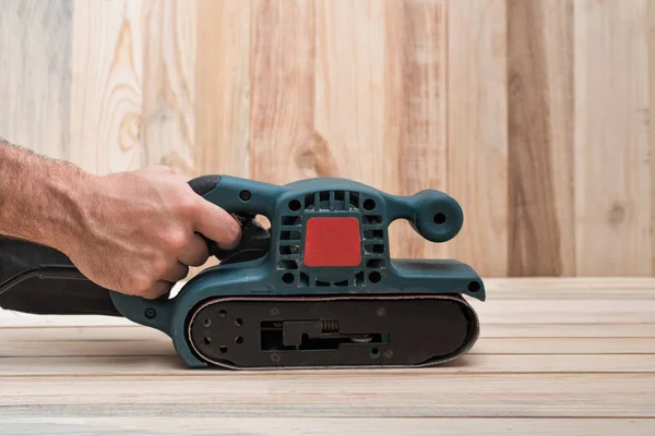 Electric belt sander, sanding machine in male hand. Processing of workpiece on light brown wooden table. Side view, close up — Stock Image Electric belt sander, sanding machine in male hand. Processing of workpiece on light brown wooden table. Side view, close up Stock Picture