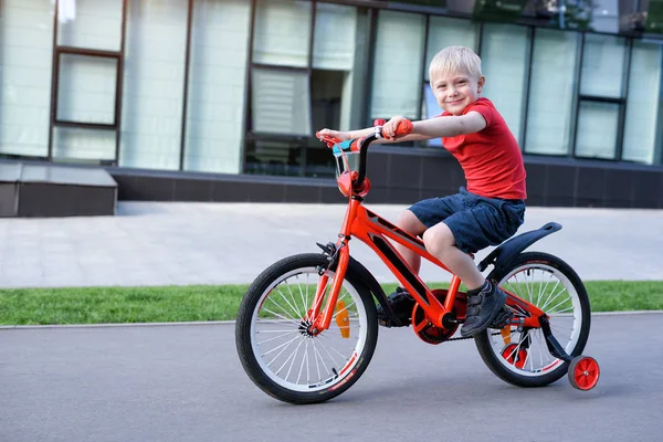 Beau garçon blond monte sur un vélo pour enfants. Contexte urbain — Photo