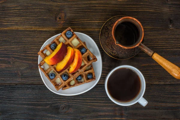 Schokolade belgische Waffeln mit Früchten, Tasse Kaffee und Cezve auf Holzuntergrund. leckeres Frühstück. Ansicht von oben — Stockfoto