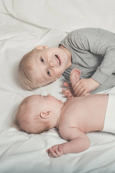 Lindo bebé y sonriente hermano mayor están acostados en la cama. Juega e interactúa. Vista superior — Foto de Stock
