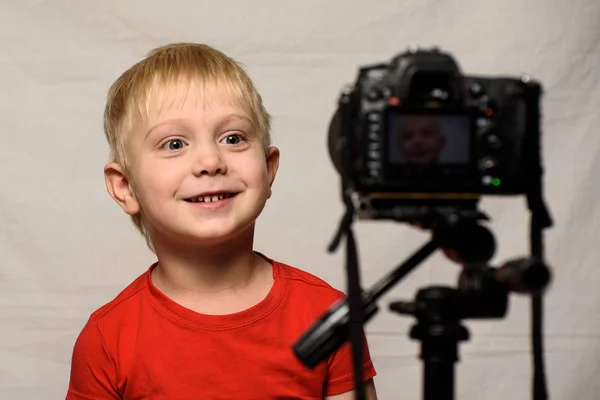 Uśmiechnięty blond chłopiec przed obiektywem aparatu. Mały blogger wideo. Studio domowe — Zdjęcie stockowe