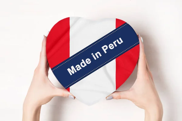 Επιγραφή Made in Περού η σημαία του Περού. Γυναικεία χέρια που κρατάνε ένα κουτί σε σχήμα καρδιάς. Λευκό φόντο. — Φωτογραφία Αρχείου