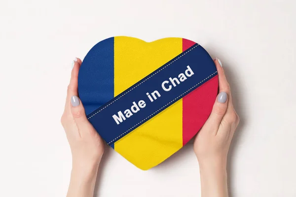 Επιγραφή Made in Τσαντ τη σημαία του Τσαντ. Γυναικεία χέρια που κρατάνε ένα κουτί σε σχήμα καρδιάς. Λευκό φόντο. — Φωτογραφία Αρχείου
