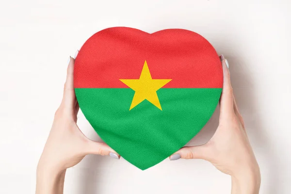 Σημαία της Μπουρκίνα Φάσο σε ένα κουτί σε σχήμα καρδιάς σε γυναικεία χέρια. Λευκό φόντο — Φωτογραφία Αρχείου
