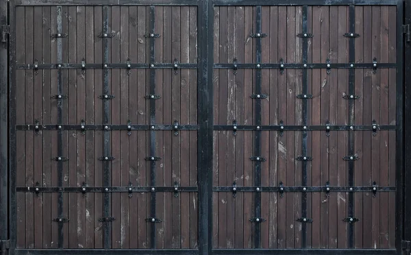 Portão de madeira marrom com listras metálicas forjadas. Fundos e texturas — Fotografia de Stock
