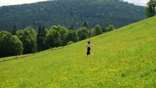 緑の山の草原を駆け下りる若い女性晴れ夏の日 遠くに森と山々 スローモーション — ストック動画