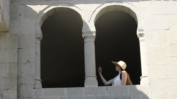 戴着帽子的年轻女子坐在旧窗户的拱门前自拍 阳光明媚的夏日 — 图库视频影像