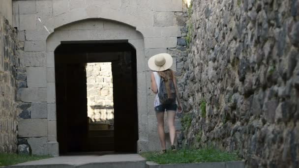 リュックサックを持った帽子をかぶった若い女性が古い建物のアーチに入る バックビュー — ストック動画