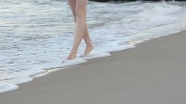 Kadın bacakları deniz boyunca yürüyor. Akşam saati
