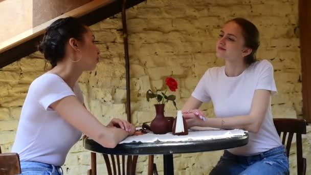 Zwei schöne Mädchen, die sich in einem Café unterhalten. Tageslicht — Stockvideo