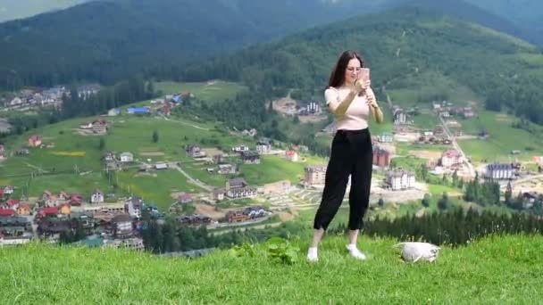 Menina morena bonita faz selfie em um fundo de montanhas. Luz do dia ventosa — Vídeo de Stock