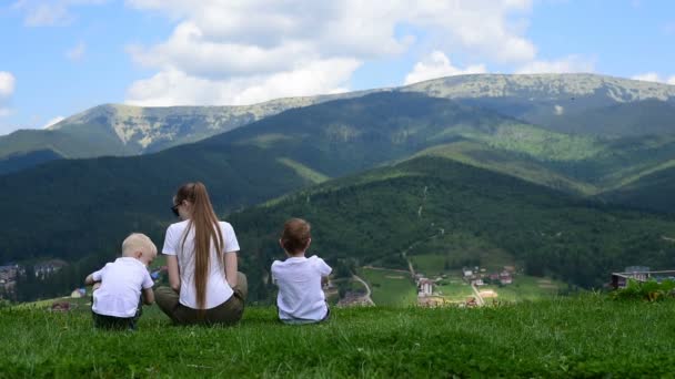 Mother and two little sons play in the meadow against the background of green forest and mountains. — Stock Video