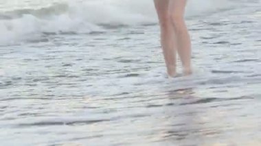 Güzel kadın bacakları sörf hattı boyunca temiz kum boyunca yürümek. Gün batımı zamanı