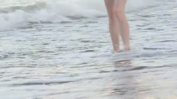 Женские ноги идут по чистому песку вдоль линии серфинга. Время заката — стоковое видео