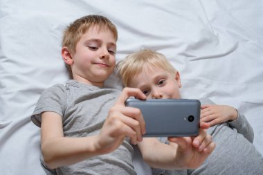 İki çocuk bir akıllı telefonla yatakta yatıyor. Gadget Eğlence