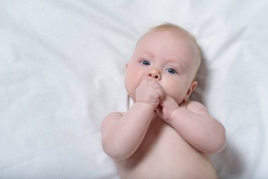 Ağızda parmakları ile sevimli bir sarışın bebek Portresi. Beyaz çarşaf. Üstte görüntü