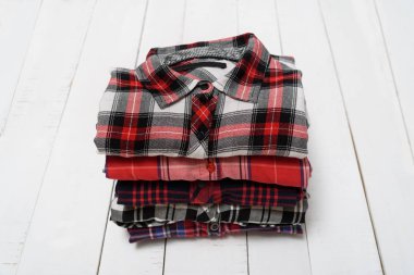 Beyaz ahşap bir arka plan üzerinde ekose gömlek yığını. Giyim konsepti.