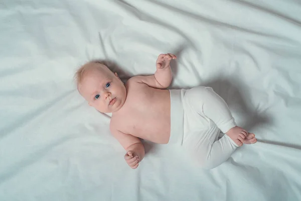 Bébé blond mignon avec un torse nu couché sur des draps blancs. Vue du dessus — Photo