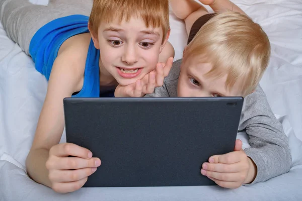 Two boys are lying in bed and looking at the tablet. Leisure gadgets — Stock Photo, Image