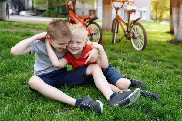 Dos chicos riéndose divirtiéndose en el césped. Bicicletas en el fondo — Foto de Stock