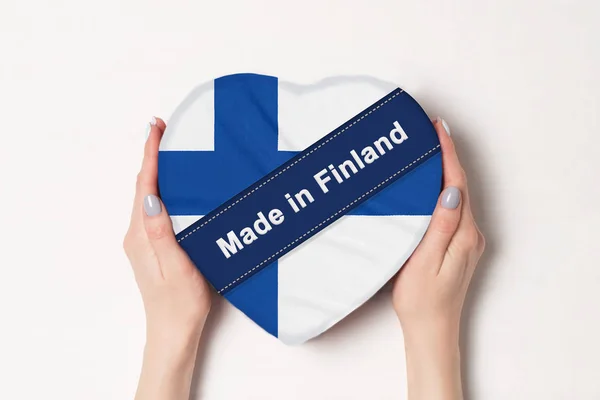 Inscripción Hecho en Finlandia la bandera de Finlandia. Manos femeninas sosteniendo una caja en forma de corazón. Fondo blanco . — Foto de Stock