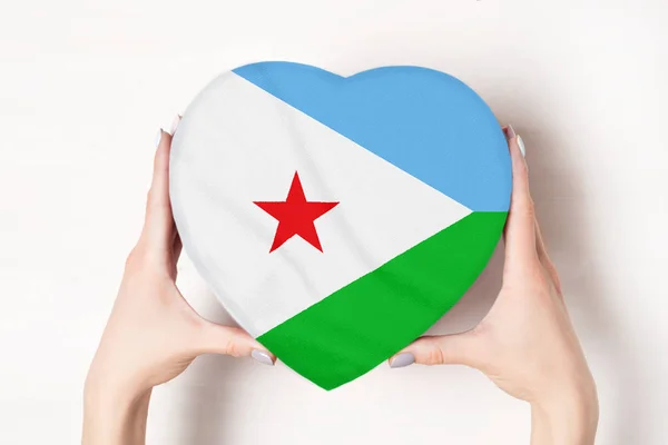 Σημαία του Τζιμπουτί σε ένα κουτί σε σχήμα καρδιάς σε γυναικεία χέρια. Λευκό φόντο — Φωτογραφία Αρχείου
