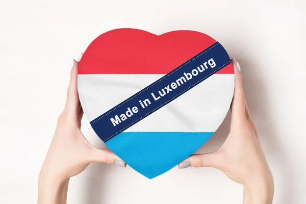 Επιγραφή Made in Λουξεμβούργο, η σημαία του Λουξεμβούργου. Γυναικεία χέρια που κρατάνε ένα κουτί σε σχήμα καρδιάς. Λευκό φόντο. — Φωτογραφία Αρχείου