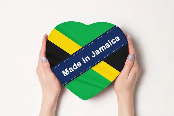 Inscripción Hecho en Jamaica la bandera de Jamaica. Manos femeninas sosteniendo una caja en forma de corazón. Fondo blanco . — Foto de Stock