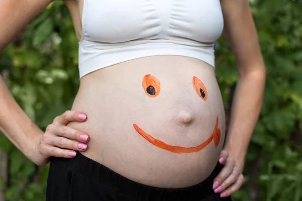 Vientre de una mujer embarazada con una cara sonriente pintada. Fondo verde — Foto de Stock