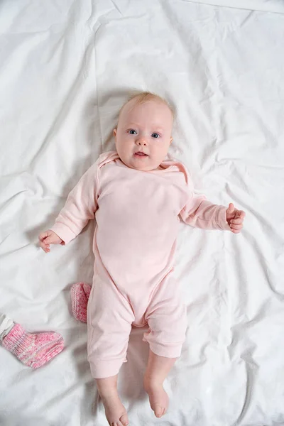 Söt baby flicka i en rosa kostym leende. Liggande på ett vitt ark — Stockfoto