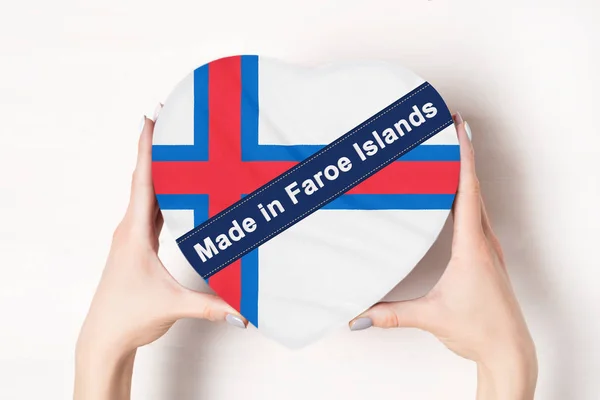 Inscrição Feita nas Ilhas Faroé, a bandeira das Ilhas Faroé. Mãos femininas segurando uma caixa em forma de coração. Fundo branco . — Fotografia de Stock
