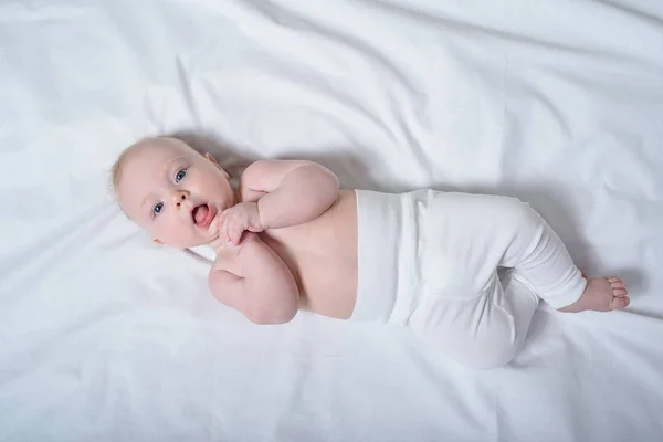 Bébé blond mignon avec un torse nu couché sur des draps blancs. Vue du dessus — Photo