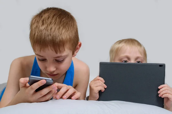 Twee jongens met gadgets liggen in bed. Kinderen gebruiken Smart Phone en Tablet — Stockfoto