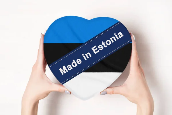 Inscrição Made in Estonia, a bandeira da Estónia. Mãos femininas segurando uma caixa em forma de coração. Fundo branco . — Fotografia de Stock