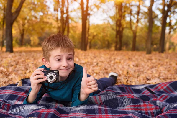 Roztomilý usměvavý kluk s kamerou leží na kostře, žlutý podzim. Den pádu — Stock fotografie