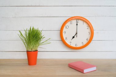 Yuvarlak duvar saati, masada pembe not defteri ve yeşil houseplant. Işyeri. İş gününün başlaması