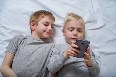 İki çocuk bir akıllı telefonla yatakta yatıyor. Gadget Eğlence
