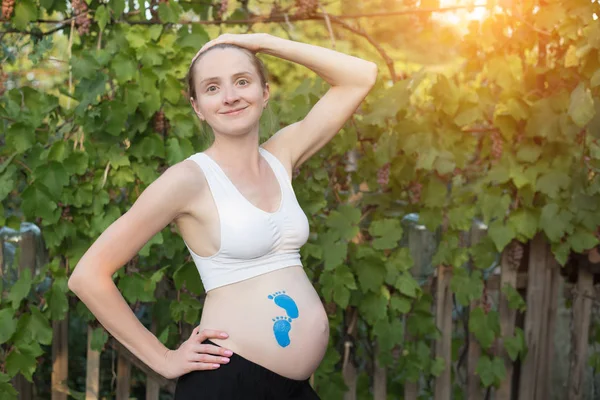 Joven mujer embarazada sonriente. Huella azul dibujando en el vientre. Concepto de embarazada . —  Fotos de Stock