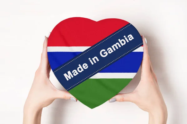 Inskriptionen gjordes i Gambia, flaggan i Gambia. Kvinnliga händer som håller en hjärtformad låda. Vit bakgrund. — Stockfoto
