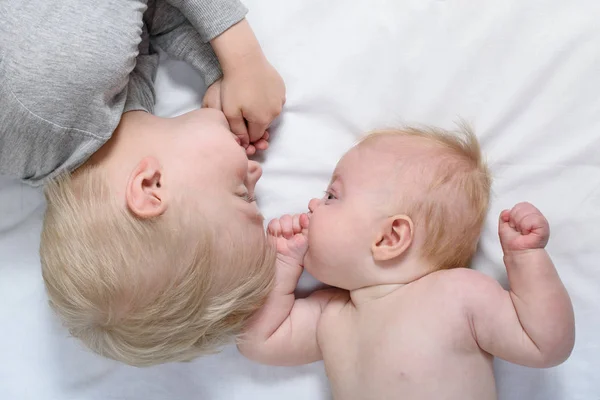 Bebé y hermano mayor sonriente están acostados en la cama. Divertido e interactuar. Vista superior —  Fotos de Stock